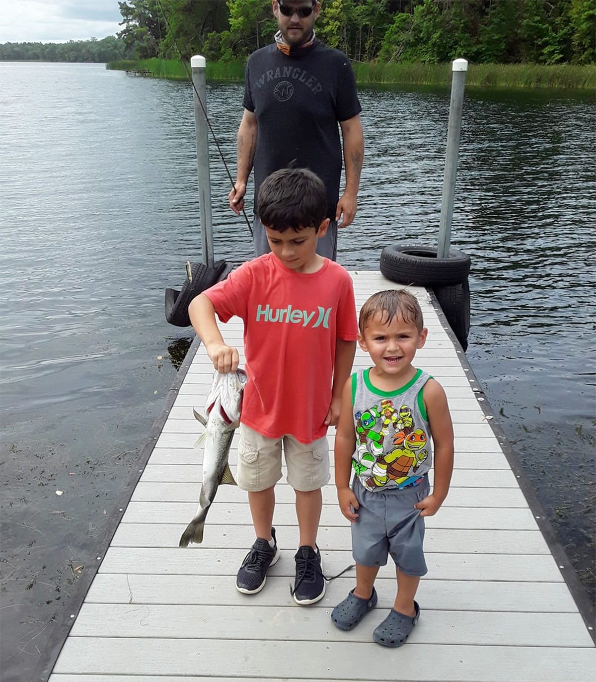 two anglers holding a largemouth bass on a dock