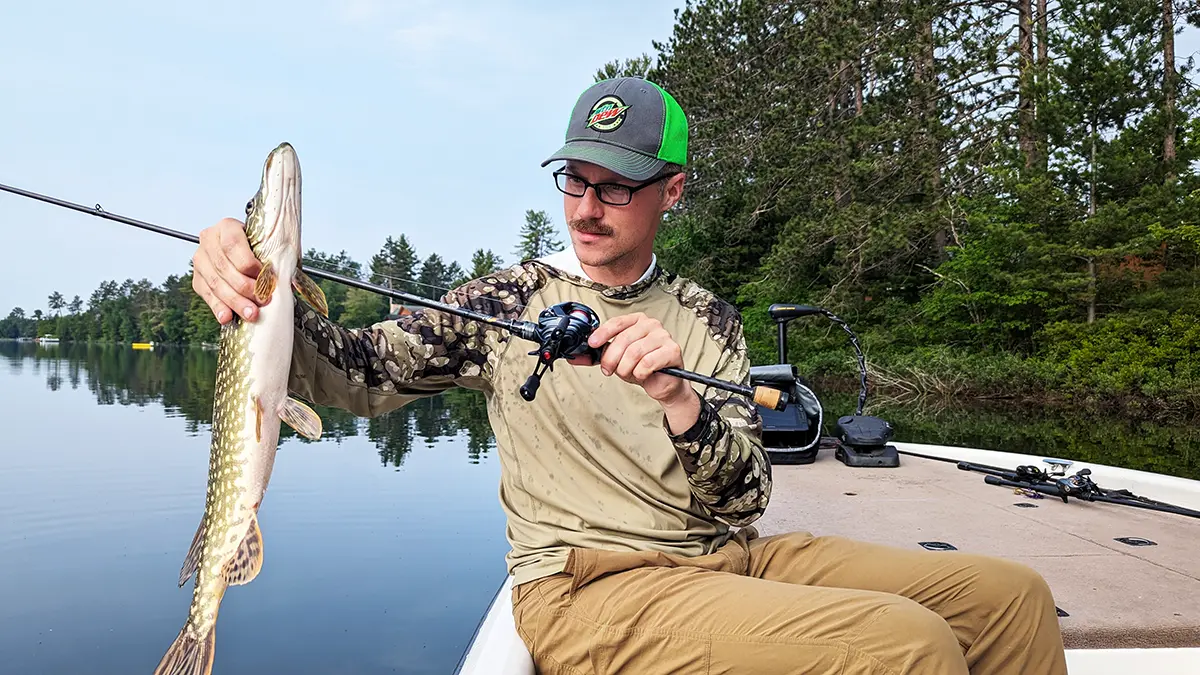 Hobie Wan Kenobi sitting in a boat holding a pike and a rod with the Daiwa Tatula BF TW 70 reel