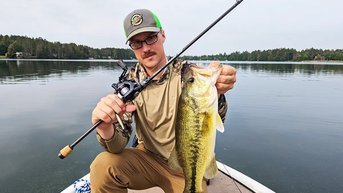 Hobie Wan Kenobi kneeling in a boat holding a bass caught using a rod with the Daiwa Tatula BF TW 70 reel