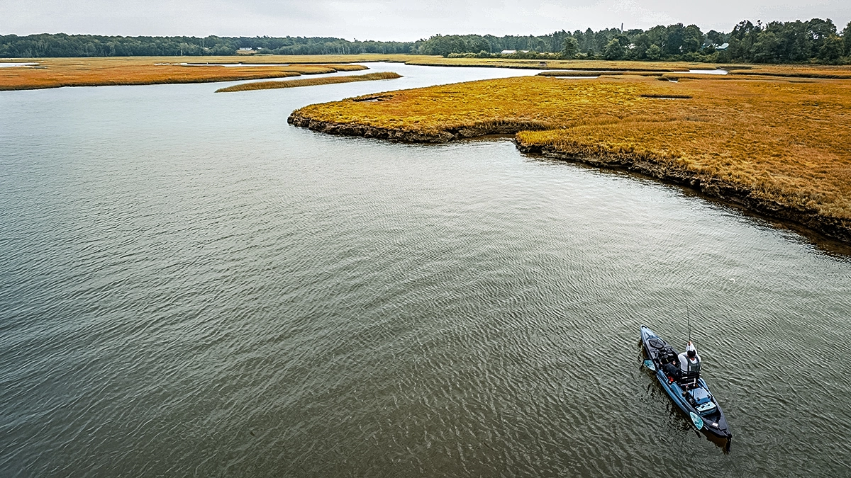 an angler in a marsky area fishing from an old town kayak