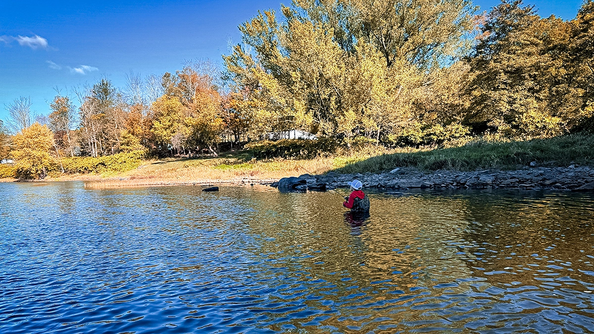 young angler standing in river in waders fishing