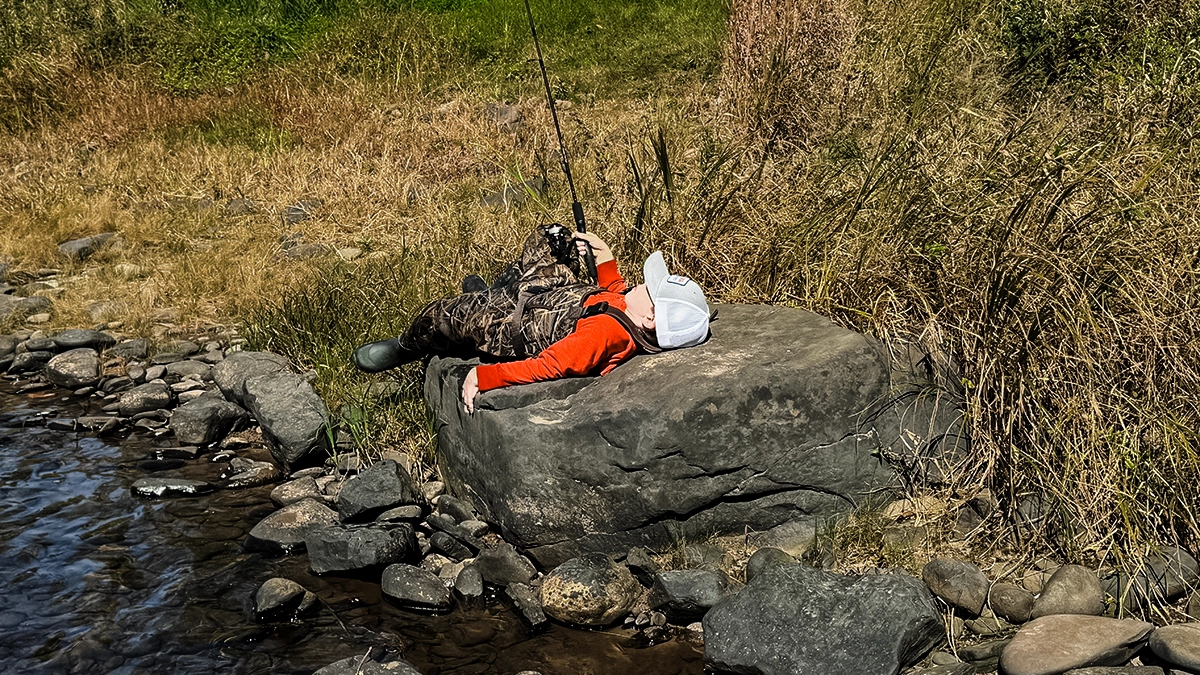 boy laying on a rock with a fishing rod