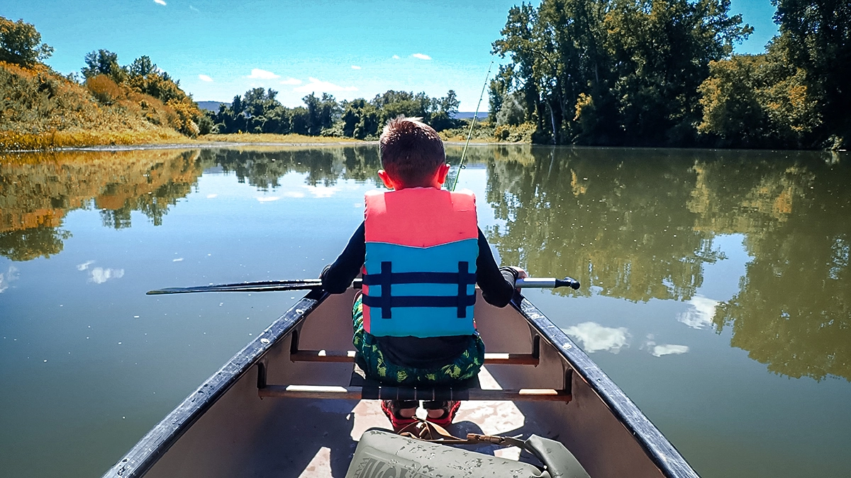 young boy sitting at front of canoe with fishing rod and paddle